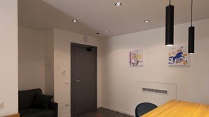 A modern room with a wooden table, a dark sofa, and a red chair. There are two black pendant lights and artwork on the wall. - Deluxe Triple Studio with Terrace (Bagheria)
