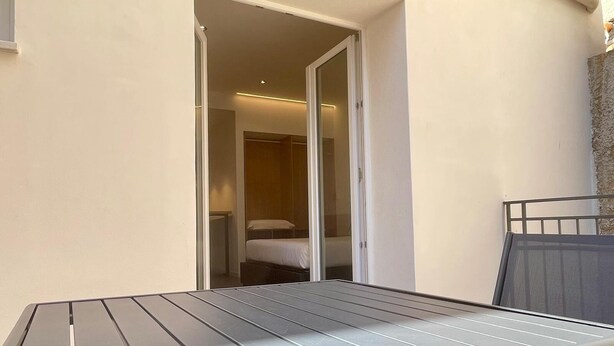 A balcony with a metal table and chairs, a sliding glass door leading to a bedroom, and a stone wall on the right. - Deluxe Triple Studio with Terrace (Bagheria)