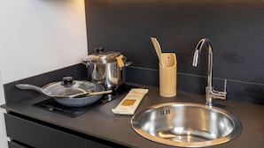 Une cuisine moderne équipée d’un évier en acier inoxydable, d’une cuisinière, d’une casserole, d’une poêle et d’un porte-ustensiles en bois.