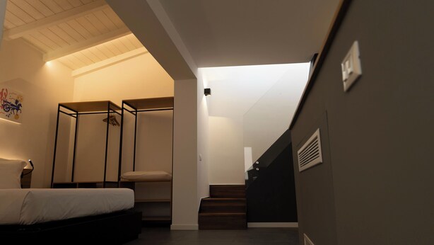 Een moderne slaapkamer met een bed, een stoel en een klein tafeltje. Er is een trap die naar een ander niveau leidt.