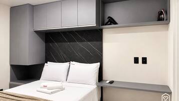 Una habitación de hotel moderna con cama, armarios grises, cabecero de mármol negro, mesita de noche con teléfono y un estante pequeño con una bolsa.