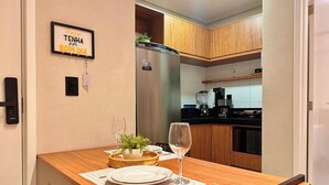 A modern kitchen with wooden cabinets, a built-in dishwasher, and a dining area with a table set for two. - Mahalo Flat - LikeHome Hospedagens (Joao Pessoa)