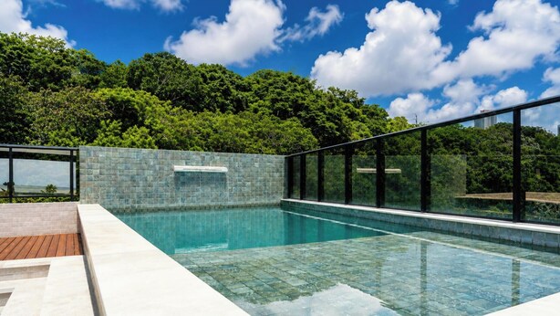 A swimming pool with glass walls, surrounded by a tiled deck, and a view of lush greenery. - Mahalo Flat - LikeHome Hospedagens (Joao Pessoa)