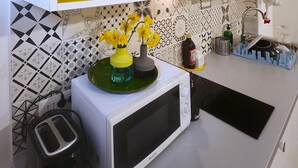 Keittiössä on mikroaaltouuni, leivänpaahdin sekä hylly, jossa on lautasia ja pullo.