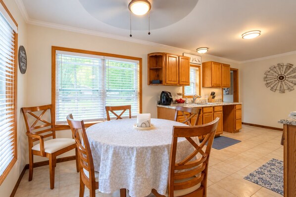 A dining area with a round table, wooden chairs, and a kitchen in the background.