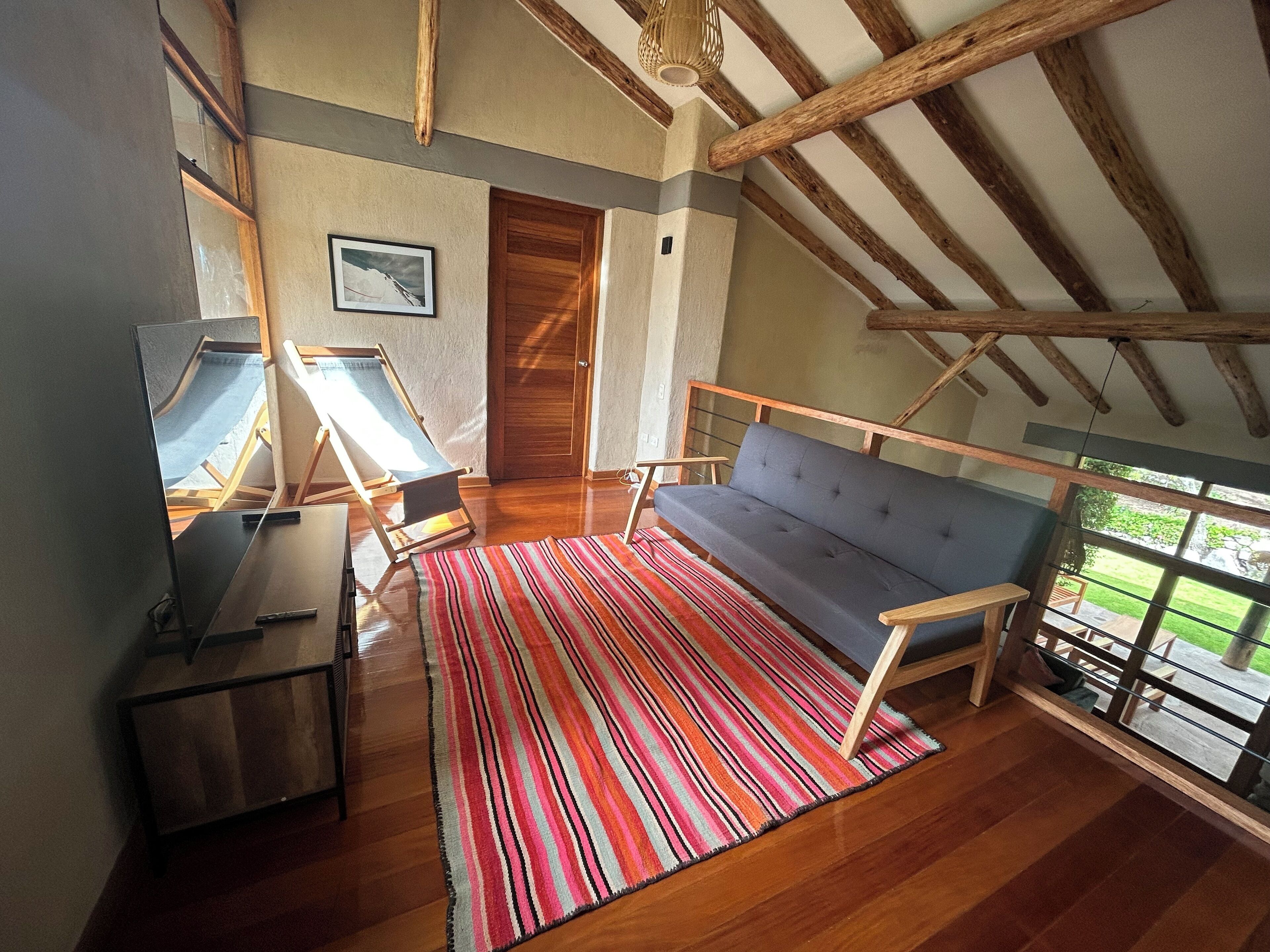 A room with a wooden ceiling, a sofa, a striped rug, and a door.