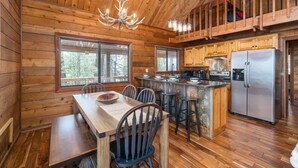 A wooden cabin interior with a dining area, kitchen, and a loft bedroom. - Ellijay Mountain View, Pets, Pool, Firepit, HotTub, Gameroom, Grill & Fireplace (Ellijay)