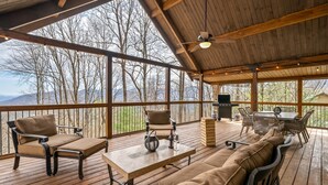 A covered outdoor deck with wooden furniture, a table, and a view of mountains. - Ellijay Mountain View, Pets, Pool, Firepit, HotTub, Gameroom, Grill & Fireplace (Ellijay)