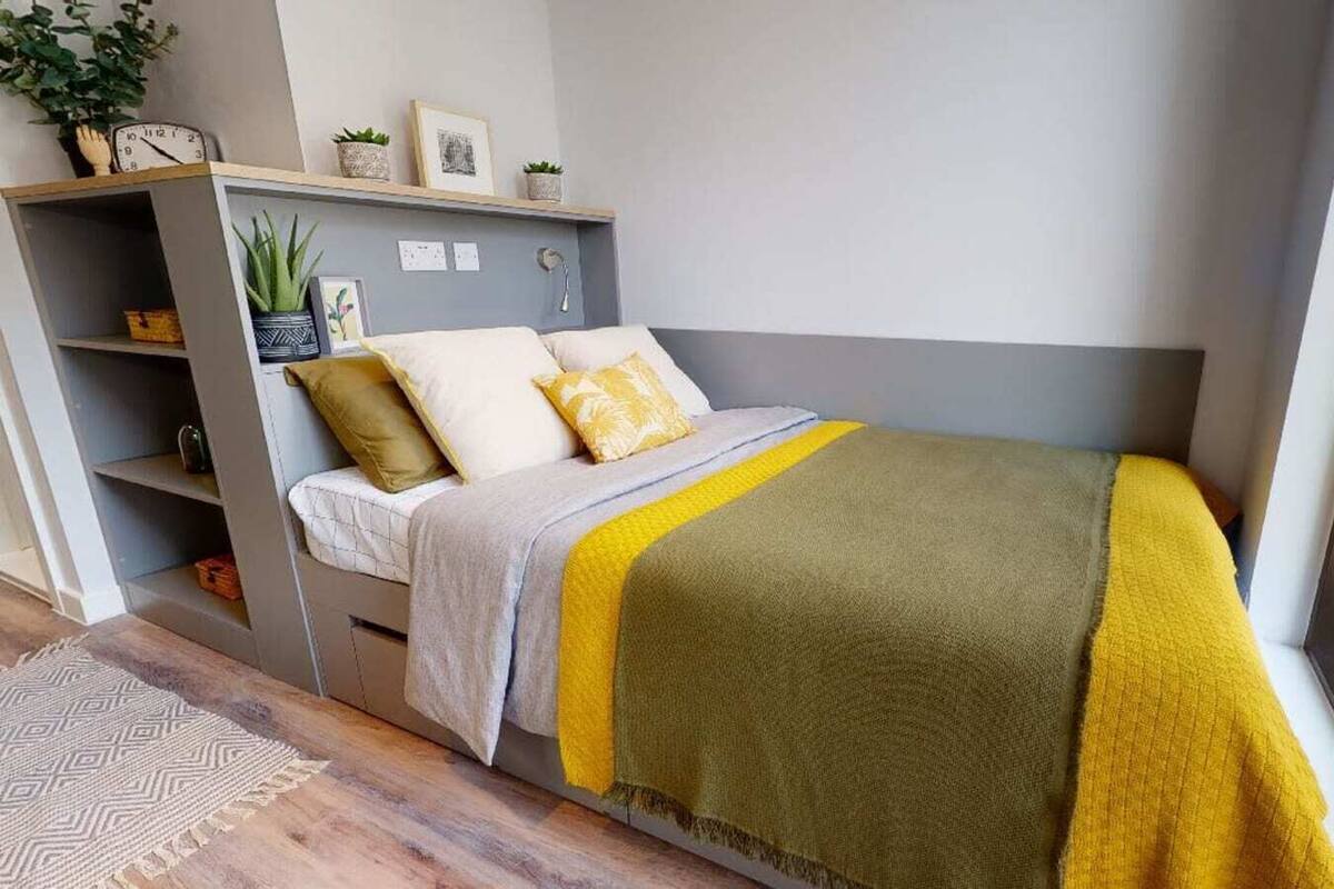 A bedroom with a bed, a bedside table, a shelf with decorative items, and a window.