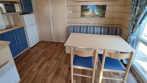 A compact kitchenette with a microwave, refrigerator, and blue cabinets. There is a wooden table with two chairs and a bench with blue cushions. A painting of the Eiffel Tower is on the wall. - Smart Home Paris mit Terrasse, Europapark, Rulantica 15min (Boofzheim)