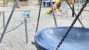 Une aire de jeux avec des balançoires, un toboggan et une structure d’escalade.