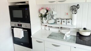 Une cuisine moderne avec des meubles blancs, un four Bosch, un micro-ondes et un plan de travail agrémenté d’ustensiles de cuisine et de boîtes de rangement.