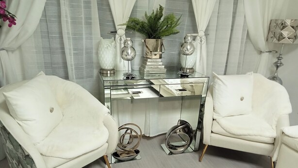 Une pièce moderne avec une table en verre, deux fauteuils blancs, un miroir et une plante en pot.