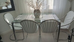 Un coin repas avec une table en verre, des chaises en métal et un vase décoré de branches.