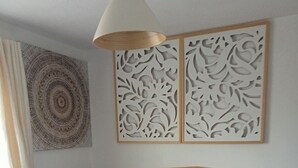 Un lit bien fait, avec une couette blanche et un plaid rouge, une tête de lit en bois et un panneau décoratif au-dessus.
