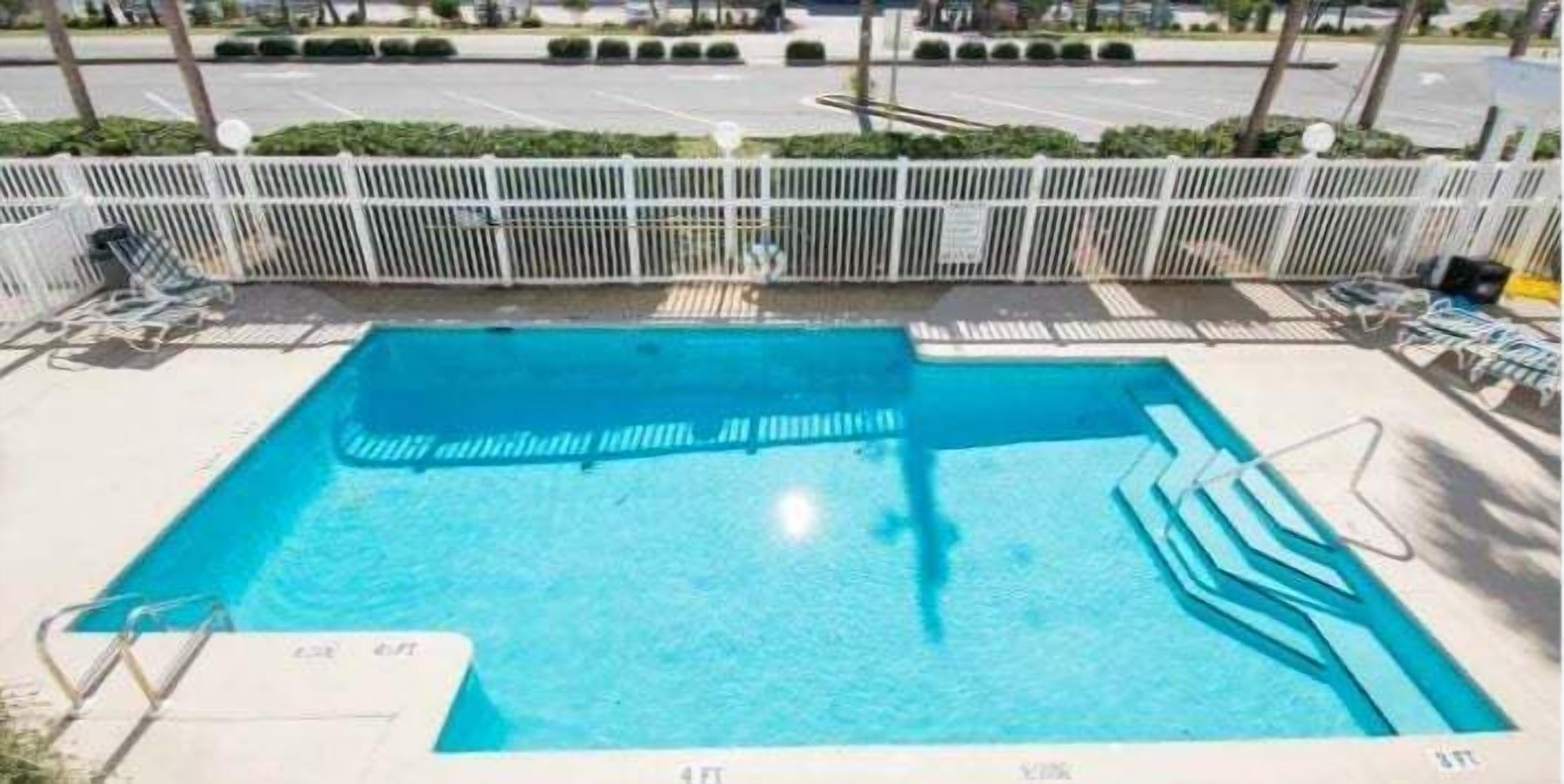 A rectangular pool with a white deck and a white fence surrounding it.