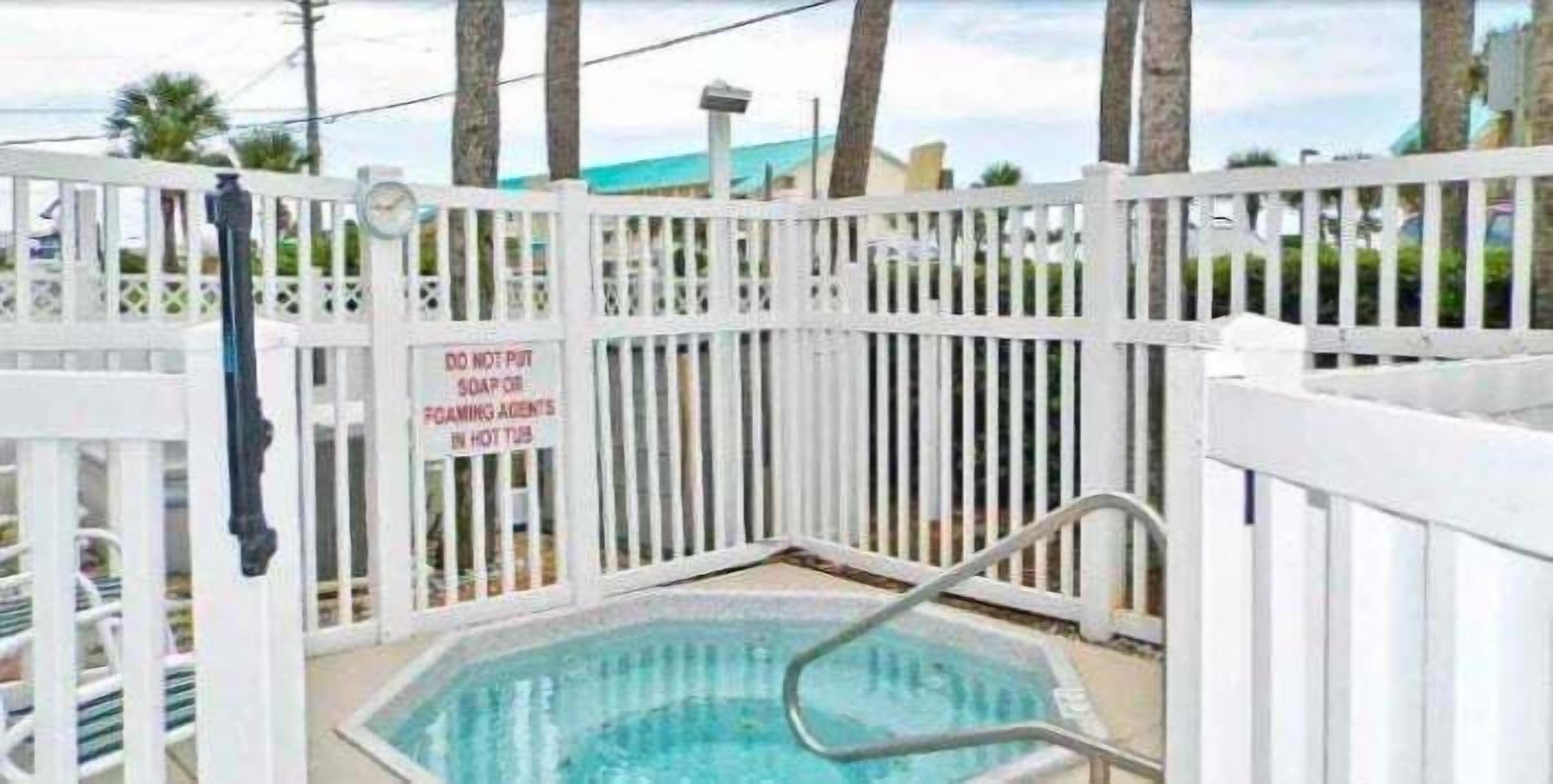 Una piscina con cerca blanca y un letrero que dice 'NO USAR SABÓN NI PRODUCTOS ESPUMANTES EN EL JACUZZI'.