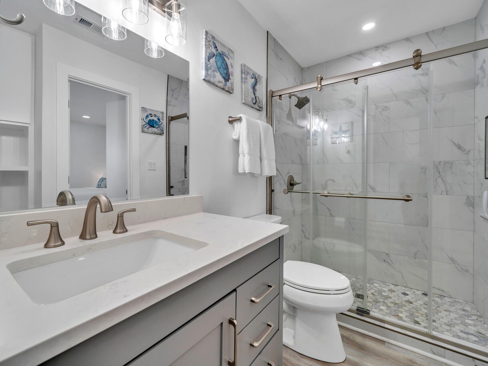 A modern bathroom with a large mirror, a sink with three faucets, a toilet, and a glass-enclosed shower area.