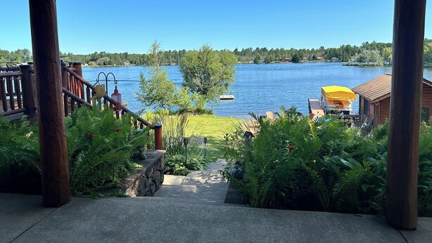 A wooden deck with a view of a lake, a boat, and a covered area with a yellow canopy. - Spacious 5-bedroom lakefront house in charming Vulcan with WiFi, AC (Vulcan)