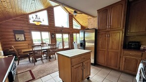 A cabin-style kitchen with wooden cabinets, a central island, and a dining area with a table and chairs. - Spacious 5-bedroom lakefront house in charming Vulcan with WiFi, AC (Vulcan)