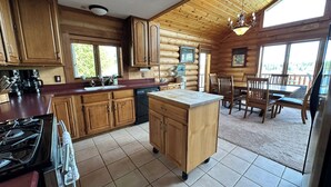 A log cabin kitchen with wooden cabinets, a stove, a dishwasher, and a dining area with a table and chairs. - Spacious 5-bedroom lakefront house in charming Vulcan with WiFi, AC (Vulcan)
