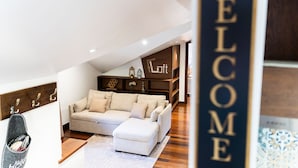 Una sala de estar moderna con sofá, reposapiés y una estantería de madera.