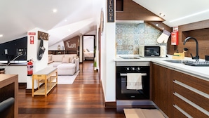 Una cocina moderna con horno integrado, microondas y lavavajillas. En la zona de estar contigua, hay un banco de madera y un sofá.