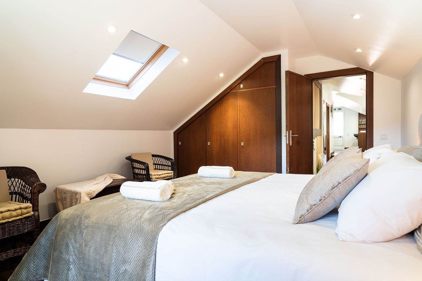 Un dormitorio con tragaluz, una cama con almohadas, una silla y un armario de madera.