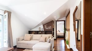 Un dormitorio tipo loft moderno con techo inclinado, sofá integrado, una pequeña mesa y un armario de madera.