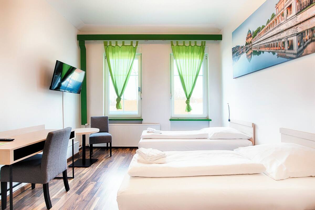 Une chambre d’hôtel avec deux lits, un bureau, une chaise, une télévision et une fenêtre avec des rideaux verts.