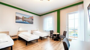 Een hotelkamer met twee bedden, een eettafel, stoelen, een schilderij en grote ramen.