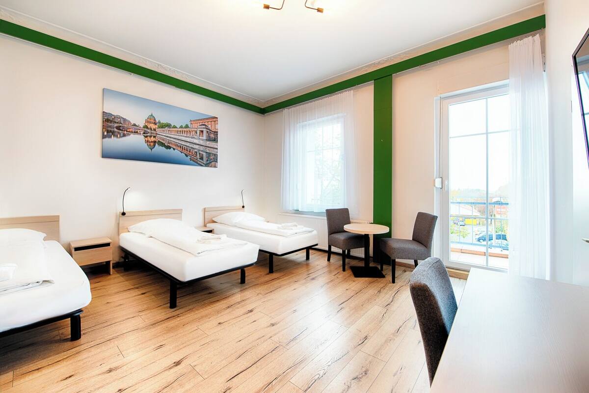 Une chambre d’hôtel avec deux lits, une table à manger, des chaises, un tableau et de grandes fenêtres.