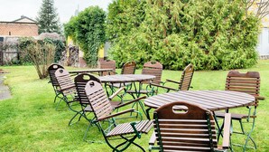 Een terras met tafels en stoelen, omringd door groen en bomen.