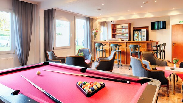 Een biljart met ballen, een bar met stoelen en een televisie aan de muur.