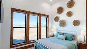 A bedroom with a bed, a ceiling fan, a large window, and a view of the outdoors. - Sunday House at The Sanctuary (Gillespie County)