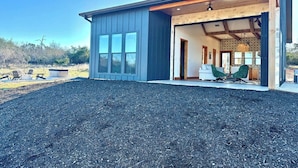A modern house with a garage, a covered outdoor seating area, and a gravel driveway. - Sunday House at The Sanctuary (Gillespie County)