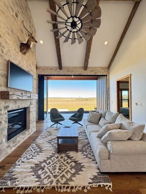 A spacious living room with a fireplace, a large sofa, and a view of the countryside. - Sunday House at The Sanctuary (Gillespie County)