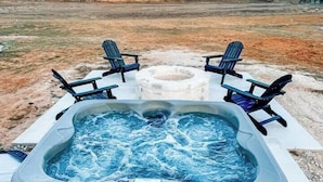 A hot tub with two chairs, surrounded by a grassy field and trees, under a clear sky. - Sunday House at The Sanctuary (Gillespie County)