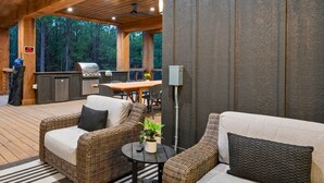 Un espacio al aire libre techado con mobiliario de mimbre, una parrilla y una mesa de comedor.