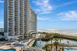 A hotel with multiple floors, a pool area, and a view of the beach. - Steps to the Sand, Endless Ocean Views – Book Now! 2 bedroom, 2 full bath! (Myrtle Beach)