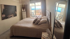 A bedroom with a large bed, a bedside table, a mirror, and a view of the outside.