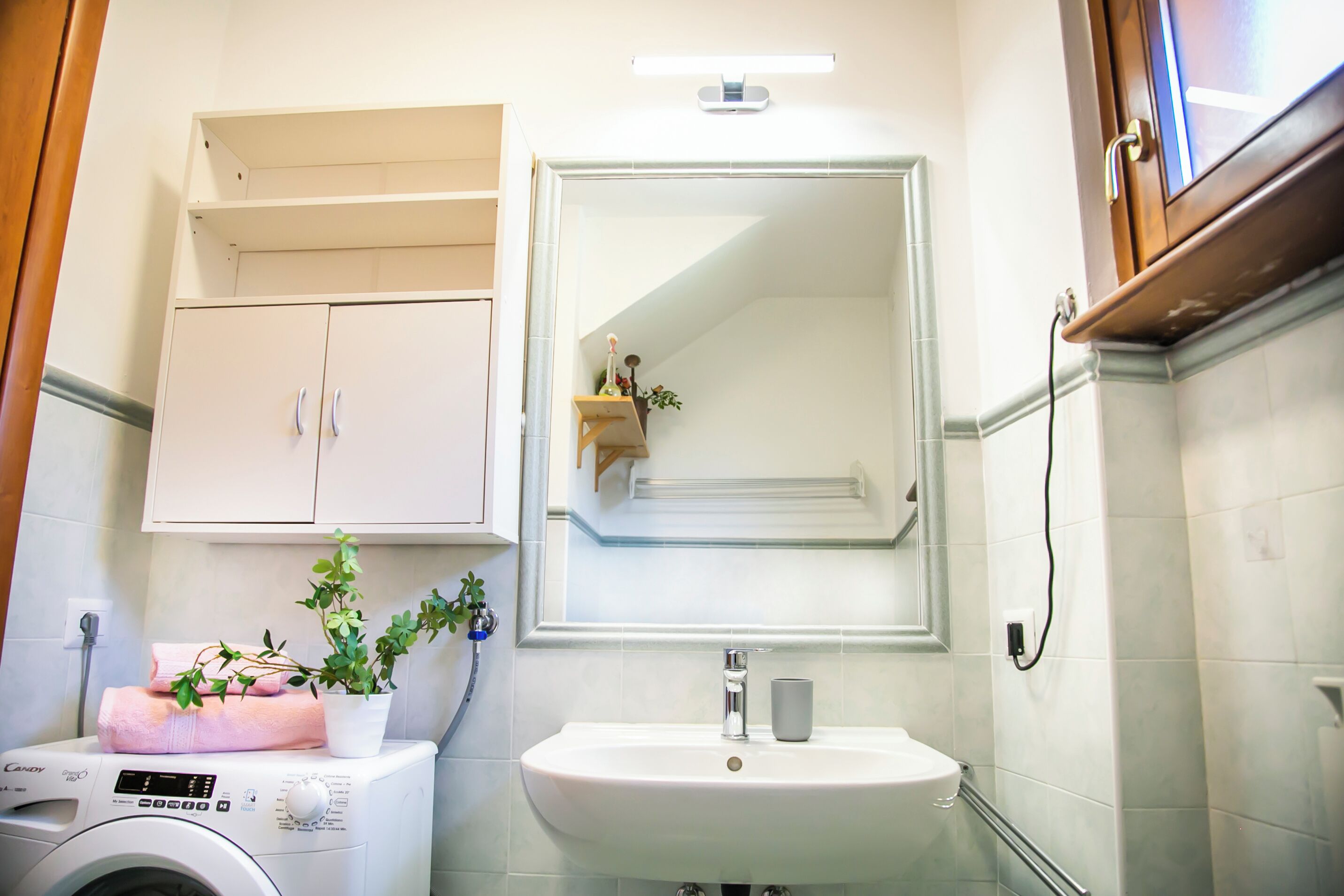 A compact bathroom with a washing machine, a sink, a mirror, and a cabinet.