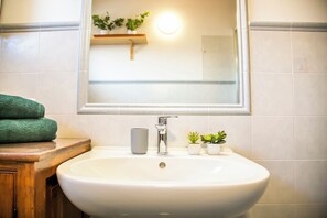 A bathroom with a white sink, a mirror, a towel, and a small plant. - Il Borghetto (Alta Valle Intelvi)