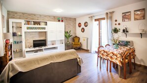 A living room with a sofa, TV, bookshelf, and dining area with chairs and a table. - Il Borghetto (Alta Valle Intelvi)