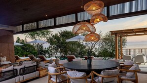 Un área de estar al aire libre con sillas y mesas de mimbre, sombrillas y vistas al mar.