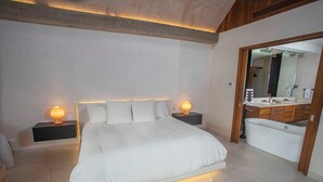 Un dormitorio con una cama grande, lámparas de noche, una tocador con espejo y una bañera.