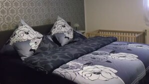 Une chambre avec un papier peint à motifs, un lit avec une literie à fleurs et un berceau dans un coin.