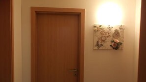 Une porte en bois fermée avec une poignée, un luminaire fixé au mur et une œuvre d’art florale.