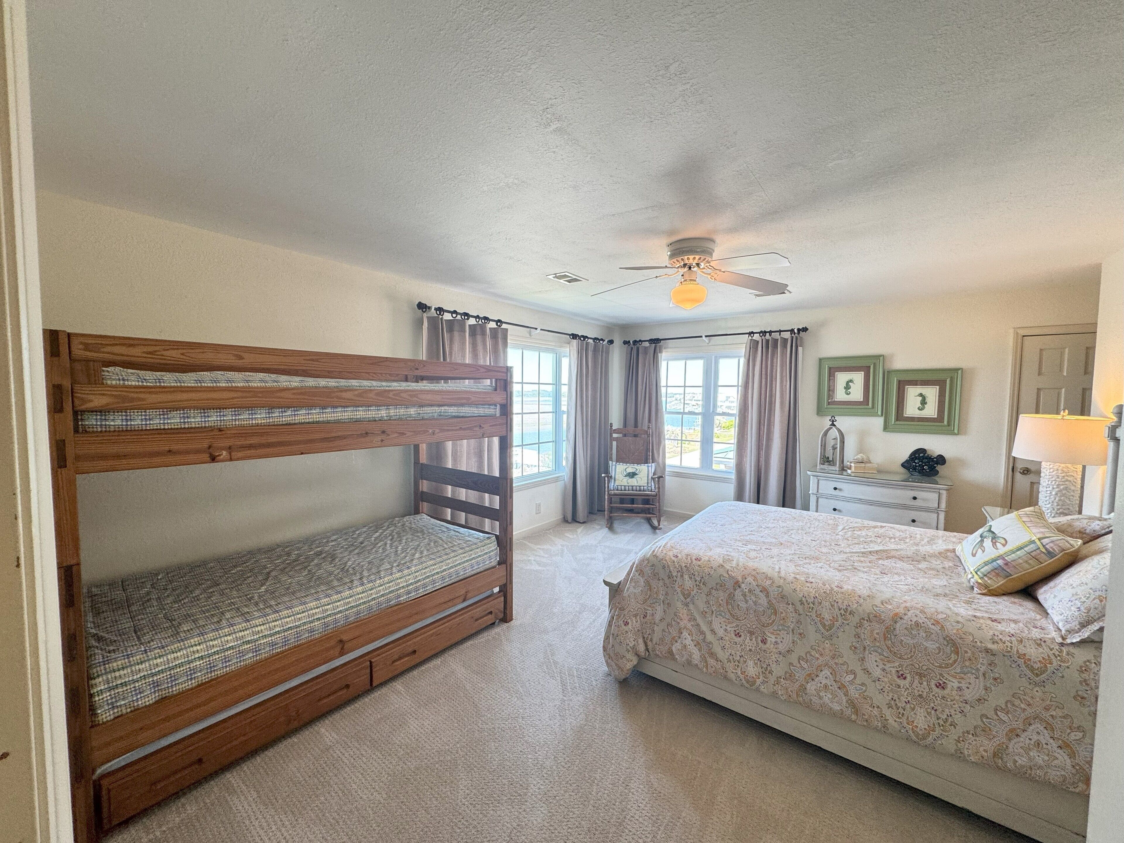 A bedroom with a bunk bed, a single bed, a chair, a dresser, and a ceiling fan.