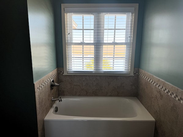 A bathroom with a bathtub, a window with blinds, and tiled walls.